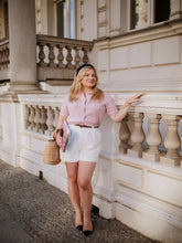 A lady wears a pink cardigan and white shorts.